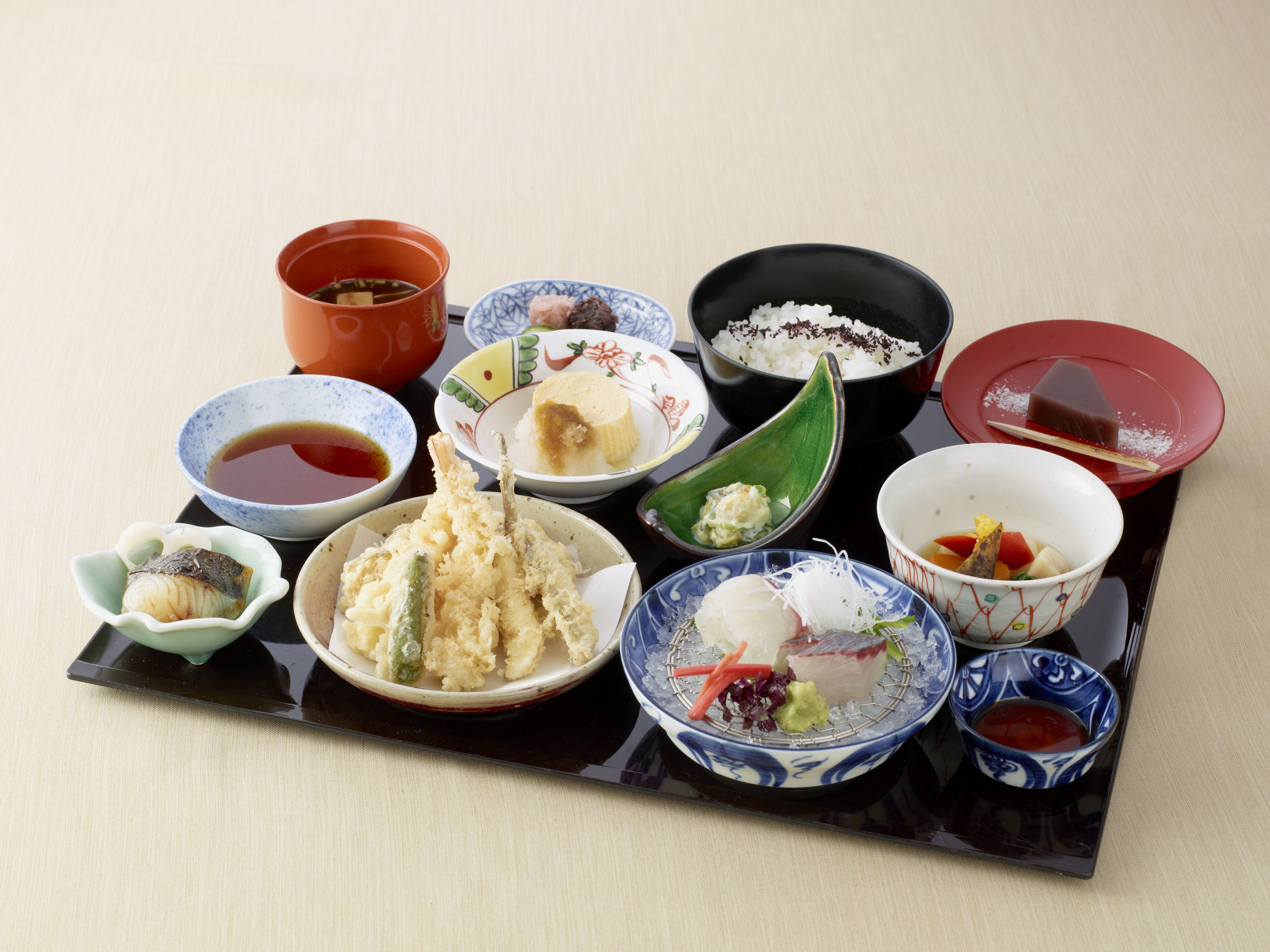 A variety of Japanese dishes arranged on a black tray.