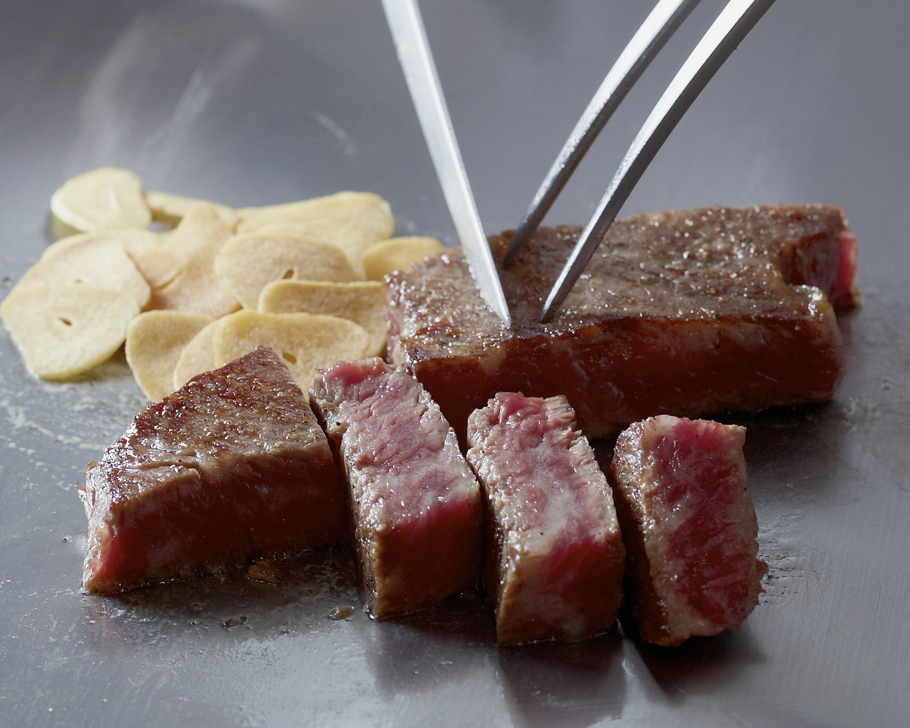 Un bistec con tenedor y cuchillo, acompañado de papas fritas.