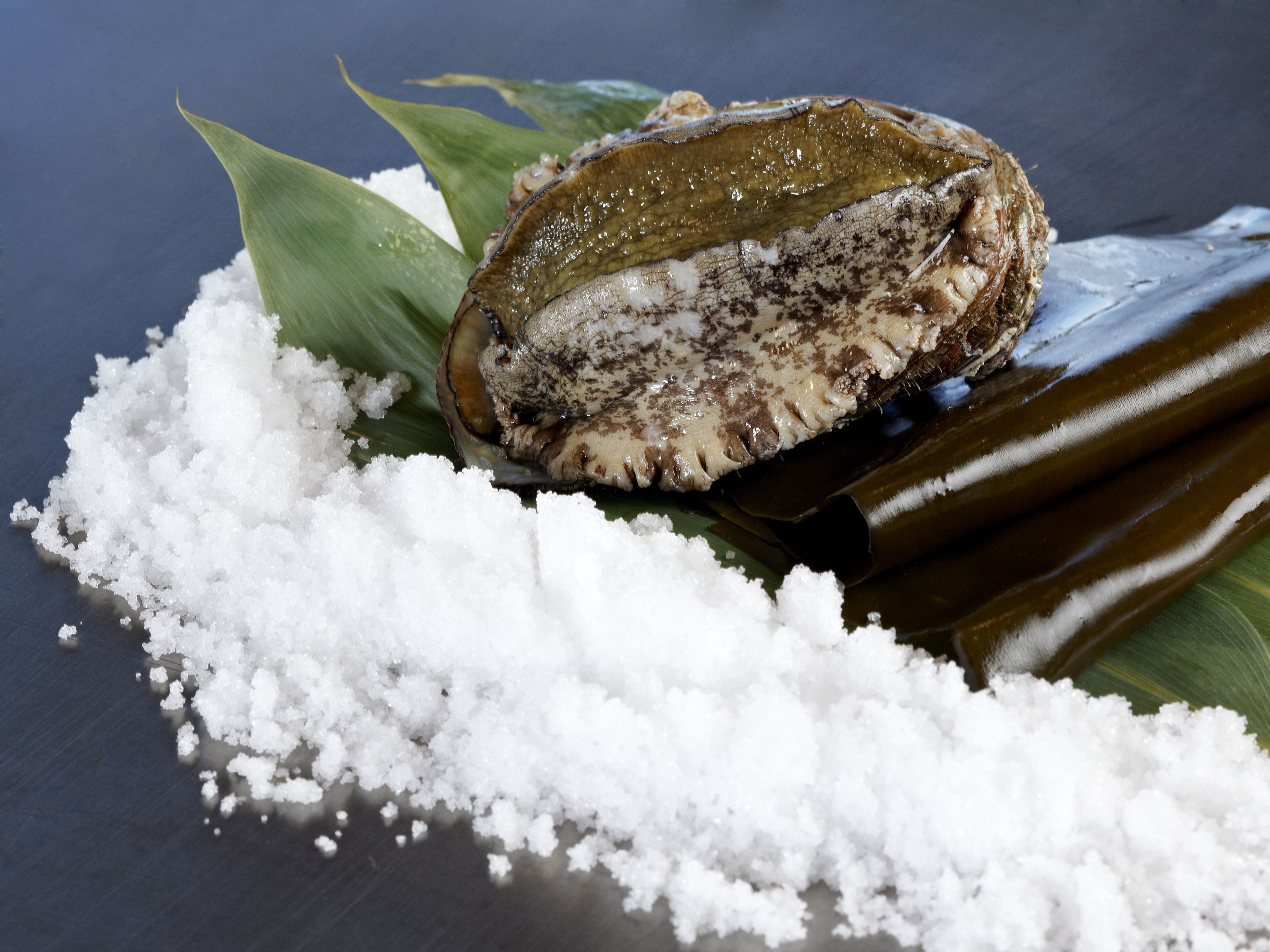 A traditional food item, possibly a sweet or savory dish, wrapped in banana leaves and accompanied by a mound of white sugar.