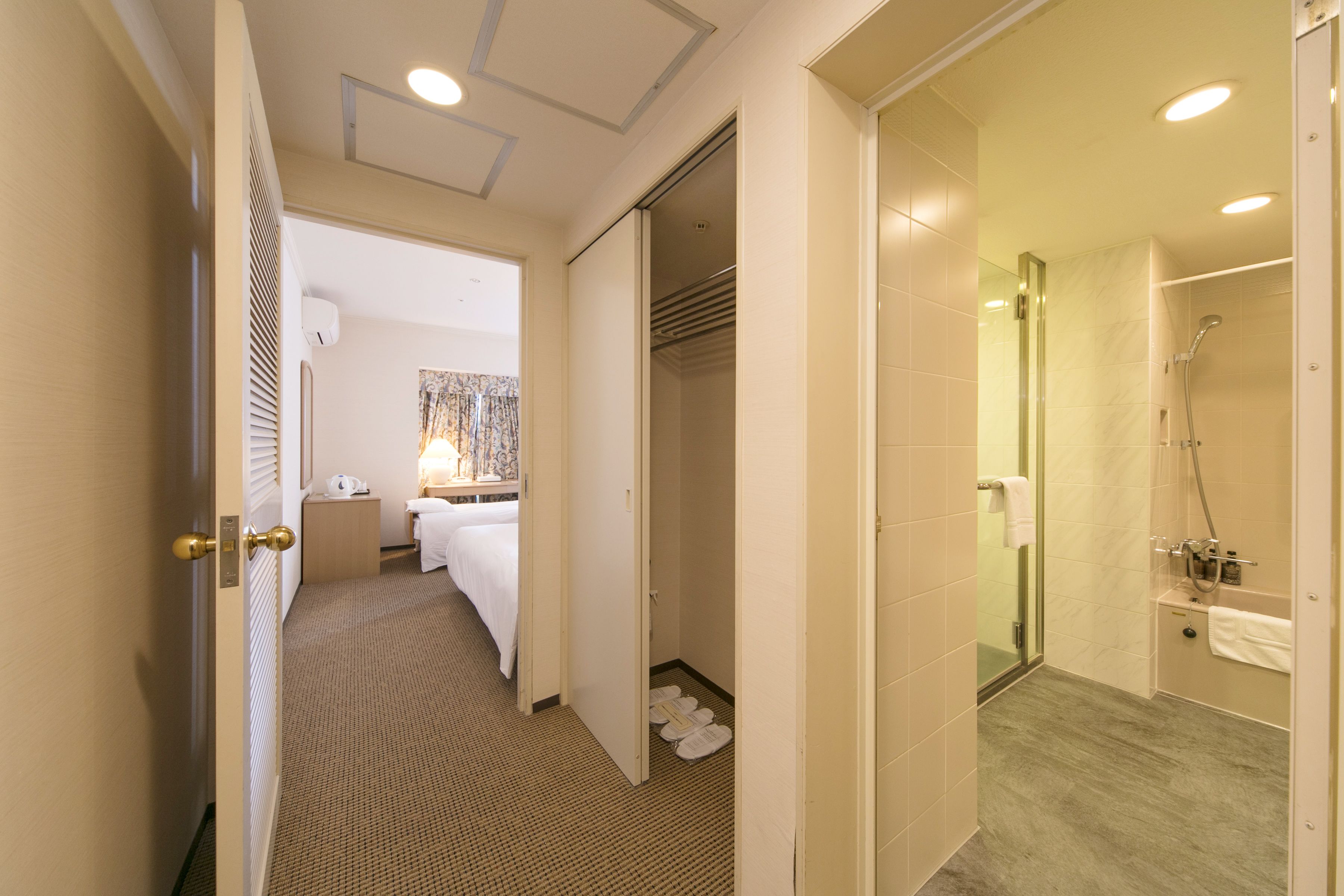 A hotel room with a bed, a bathroom with a shower, and a walk-in closet.