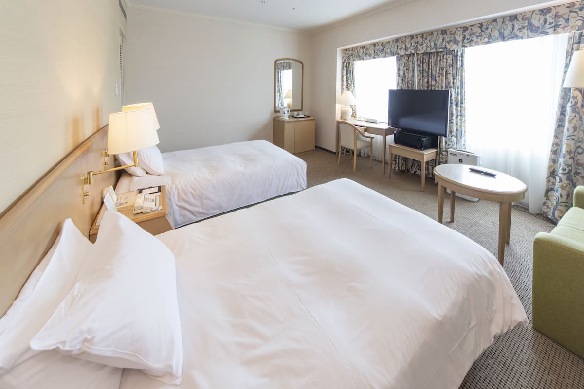 A hotel room with two beds, a desk with a television, a chair, and a small table.