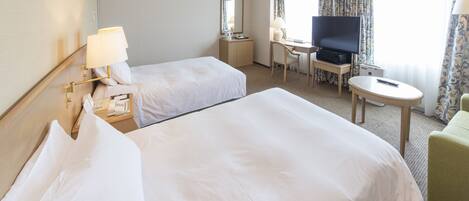 A hotel room with two beds, a desk with a television, a chair, and a small table.