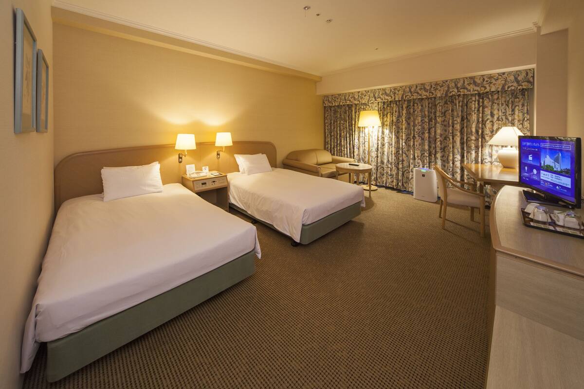 A hotel room with two beds, a desk, a chair, a television, and a desk lamp.