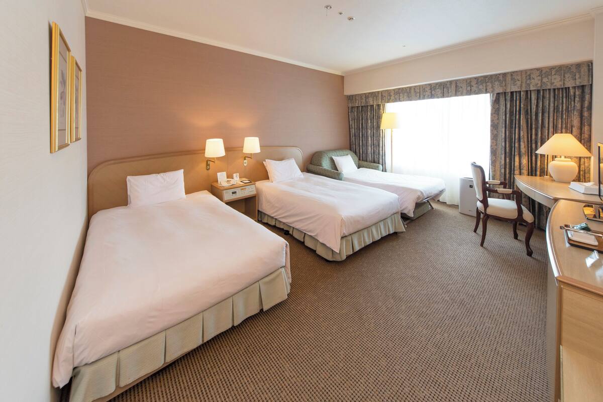 A hotel room with two beds, a desk, a chair, and a window with curtains.