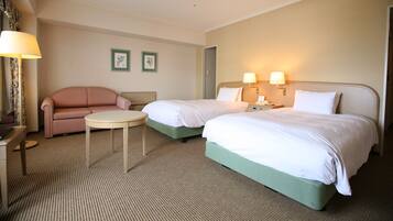 A hotel room with two beds, a sofa, a small round table, and two wall-mounted lamps.