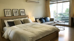 A hotel room with a large bed, a bedside table, a lamp, and a view of the outdoors through a large window. - The Link Onnut by May (Bangkok)