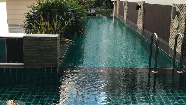 A swimming pool with clear blue water, surrounded by a modern building with multiple floors and balconies. - The Link Onnut by May (Bangkok)