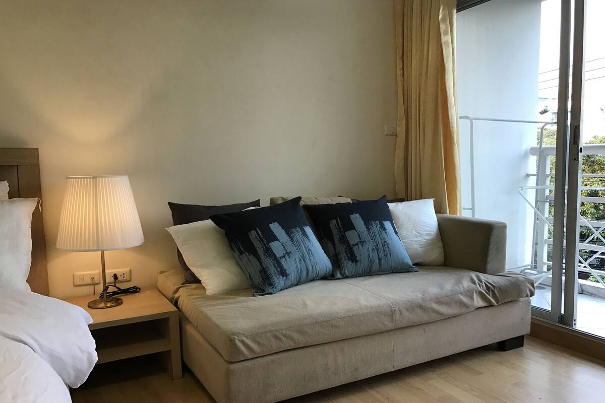 A hotel room with a bed, a sofa, a lamp, and a window with a view of the outside.