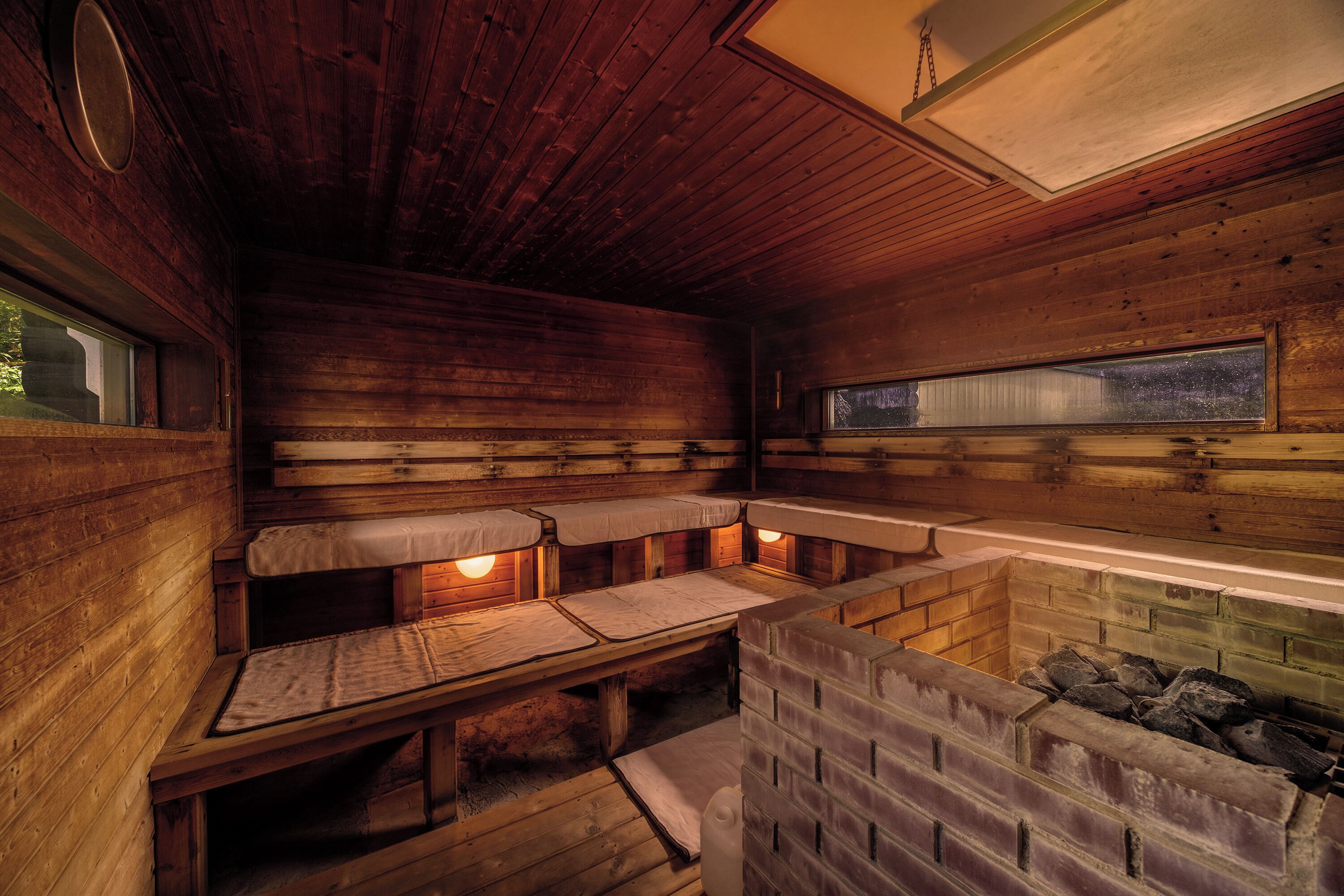 A cabin with wooden walls, a brick fireplace, and two benches with lights.