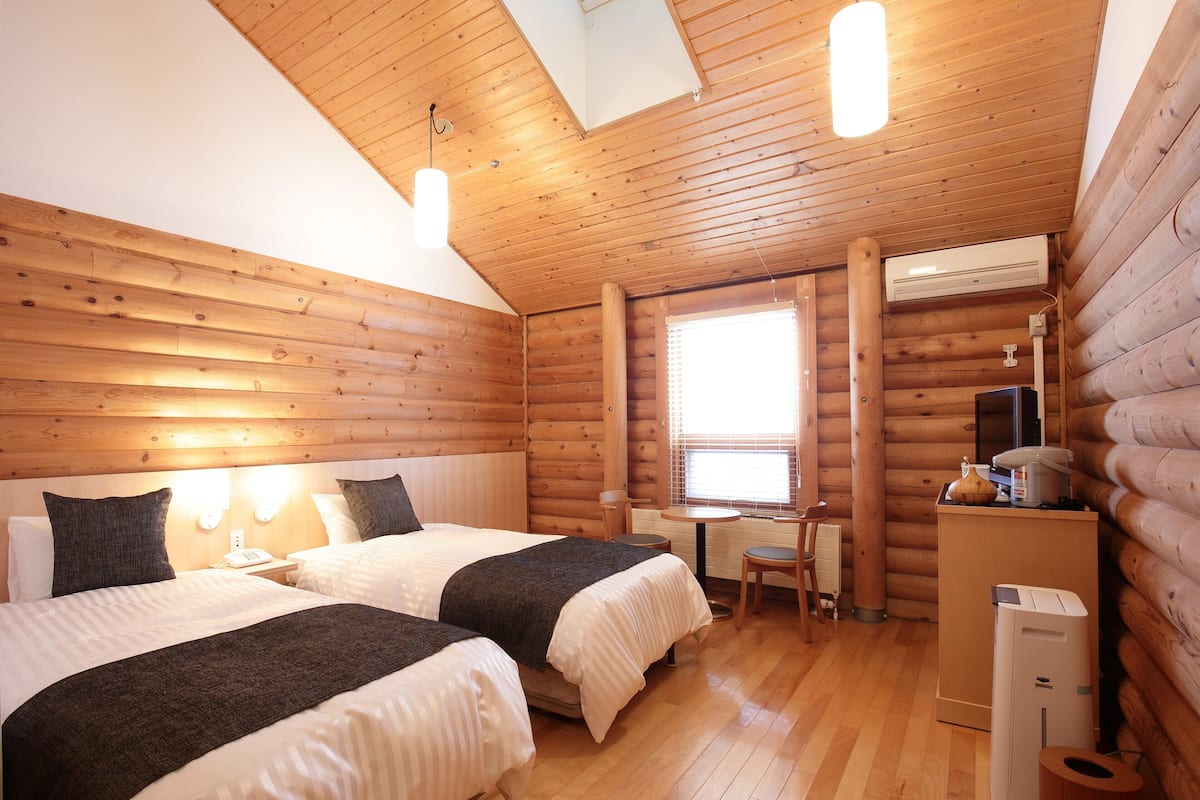Habitación tipo cabaña de madera con dos camas, un escritorio y una ventana.