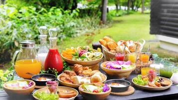 A variety of food and drinks on an outdoor table with a garden view.