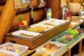 Een buffet met diverse gerechten, een rieten mand met groenten en een kaars op tafel.