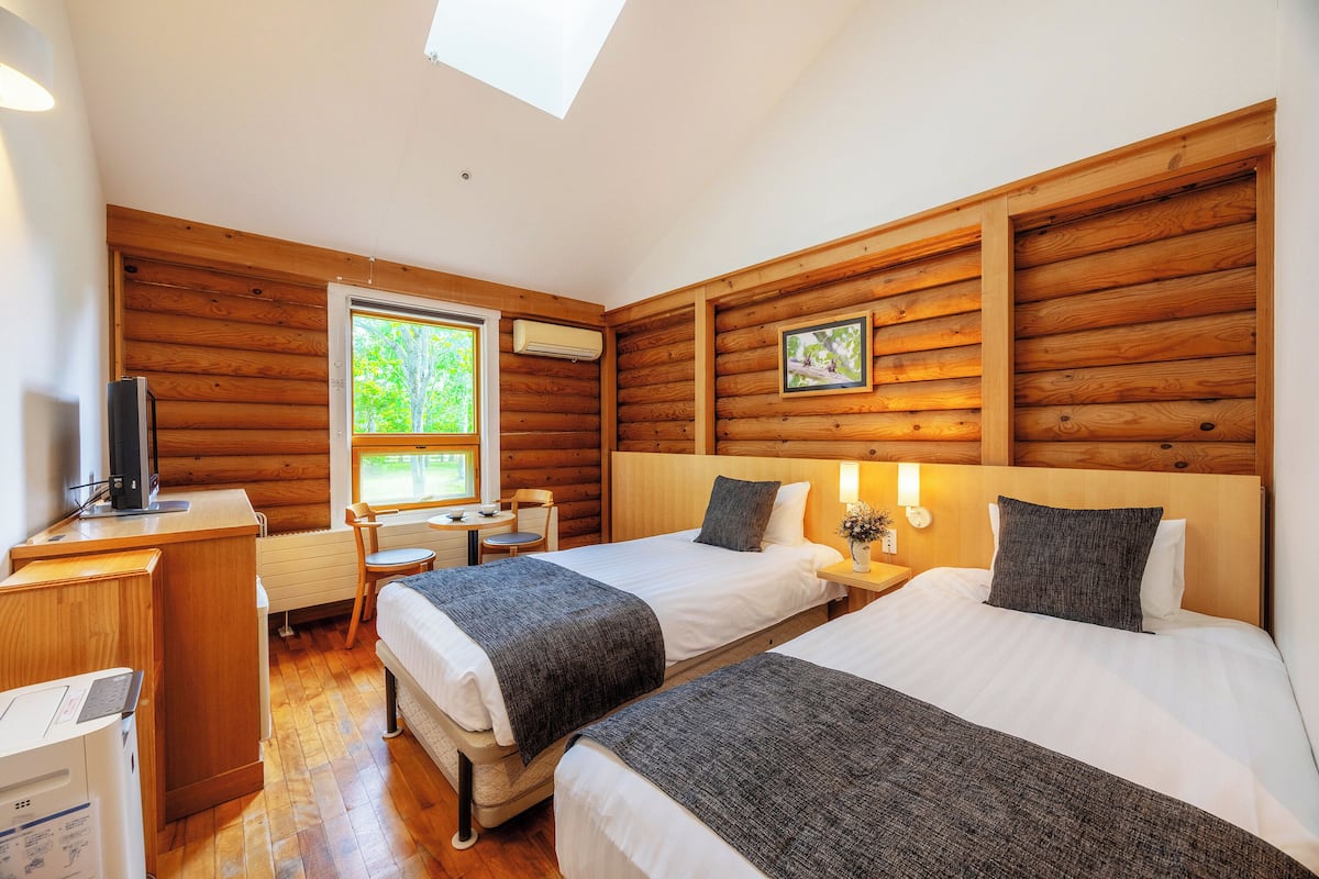 Una habitación tipo cabaña de troncos con dos camas, un escritorio, una silla y un televisor.