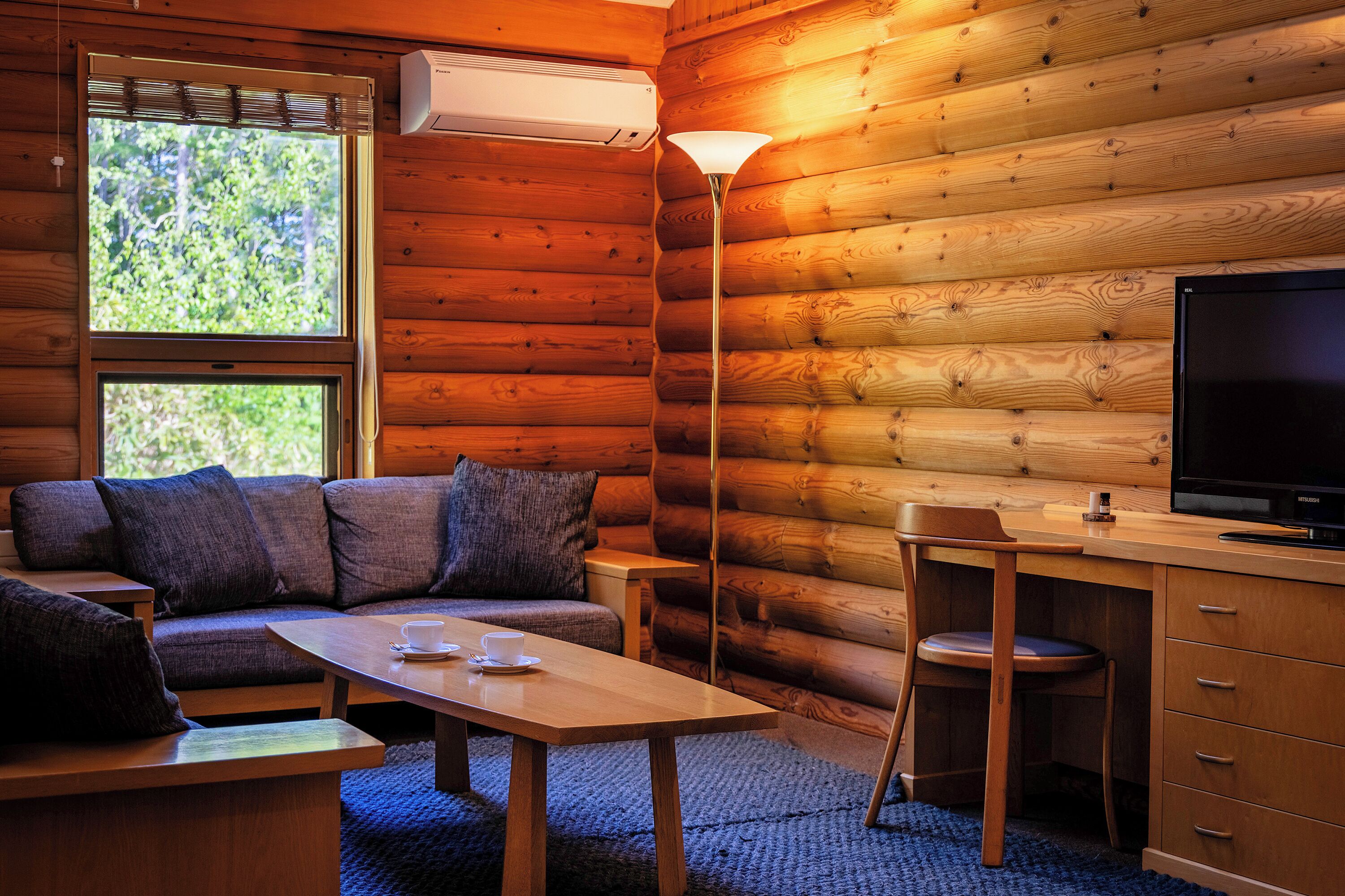 Interior de una cabaña de troncos con sofá, mesa, televisor y escritorio con cajones.
