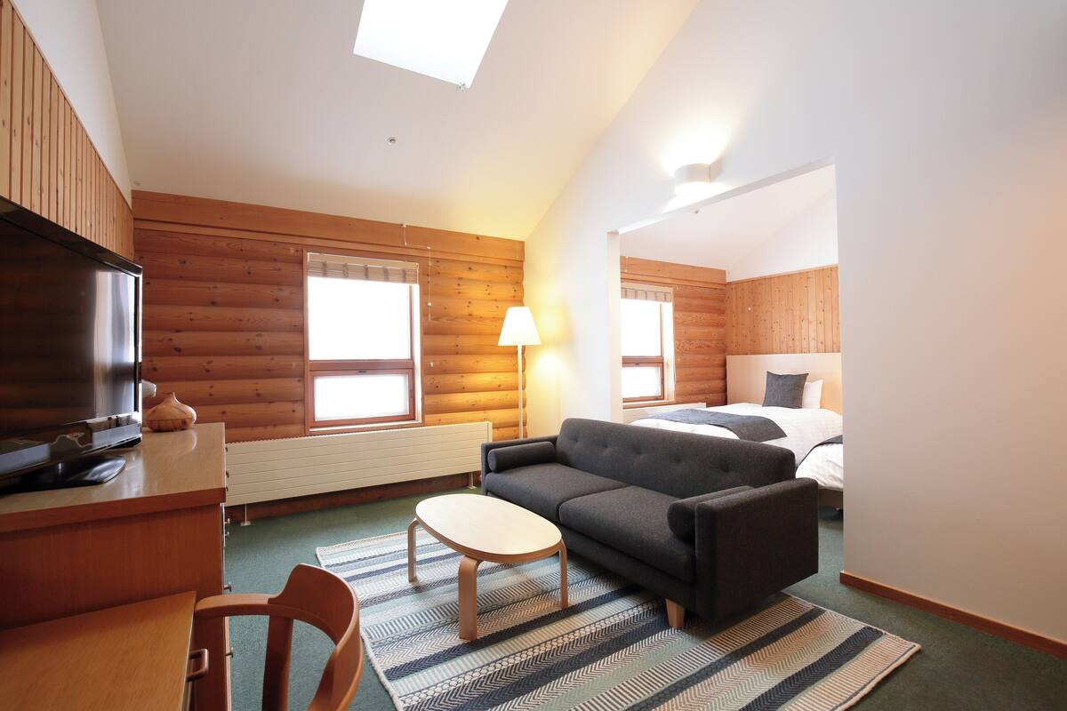 Una habitación pequeña con sofá, una mesita, televisión y cama.
