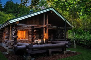 A log cabin with a porch, a table with chairs, and a window with a warm light.
