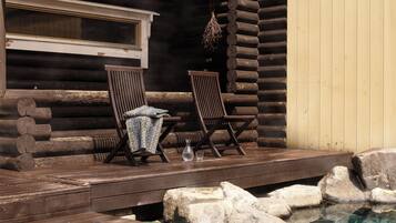 A log cabin with a wooden deck, two wooden chairs, a small table, and a clear pool with rocks.