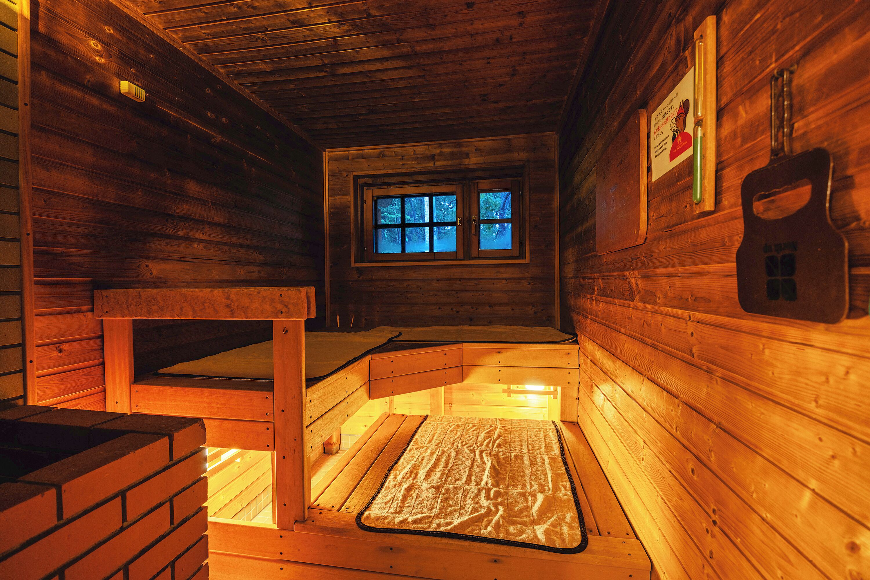 Uma cabana de madeira com uma cama de solteiro, uma janela com vista para árvores e uma parede de madeira com uma guitarra pendurada.