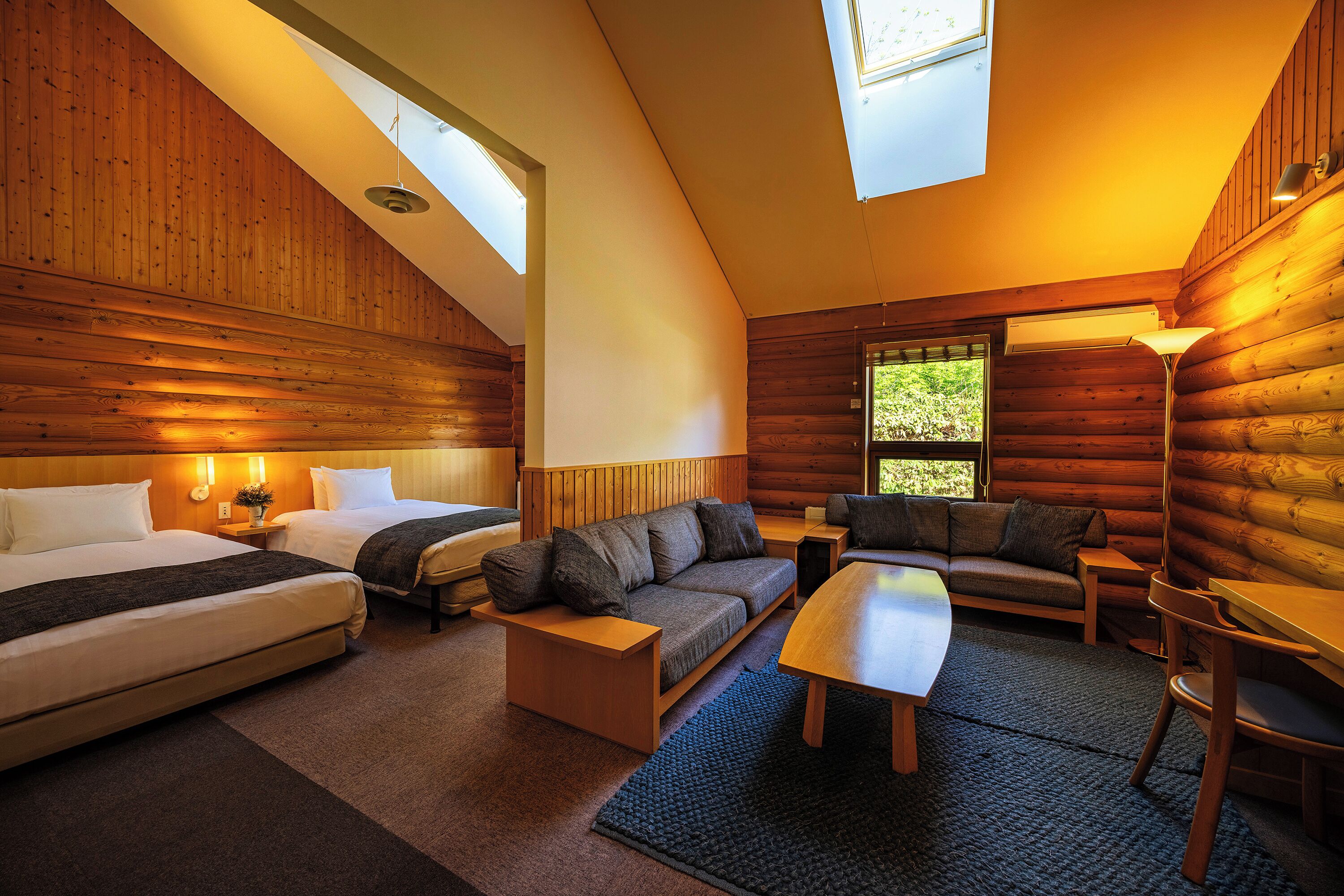 A log cabin interior with a loft bedroom, a sofa, a dining table, and a lamp.