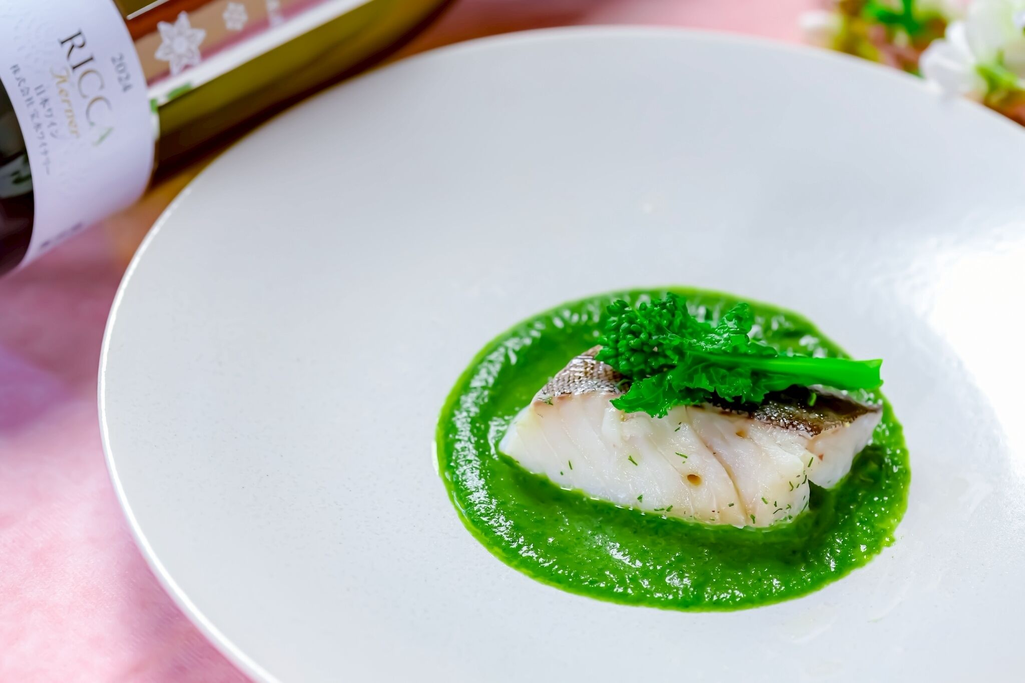 A white plate with a piece of fish and green sauce, a bottle, and a menu.