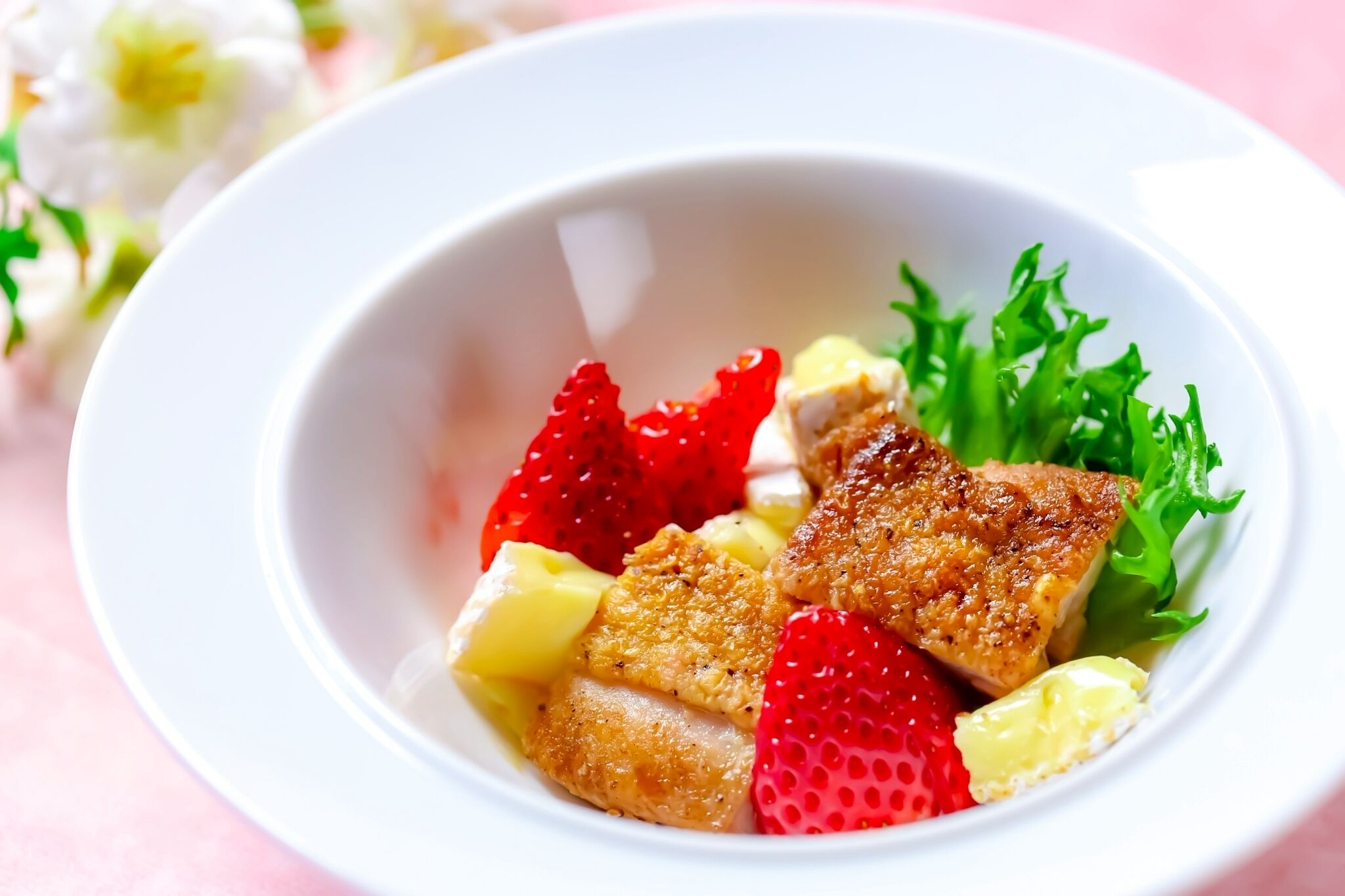 A bowl of food with strawberries, pineapple, and lettuce.