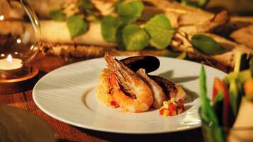 A plate with seafood and vegetables on a wooden table, surrounded by greenery and a lit candle.