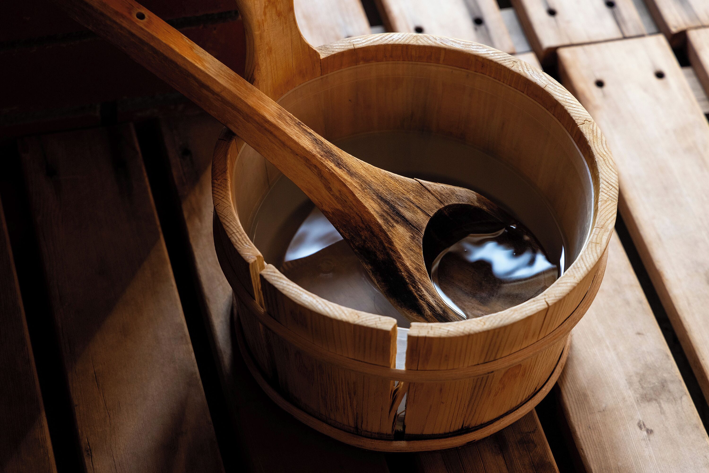 A wooden bucket with a wooden ladle inside, placed on a wooden bench.