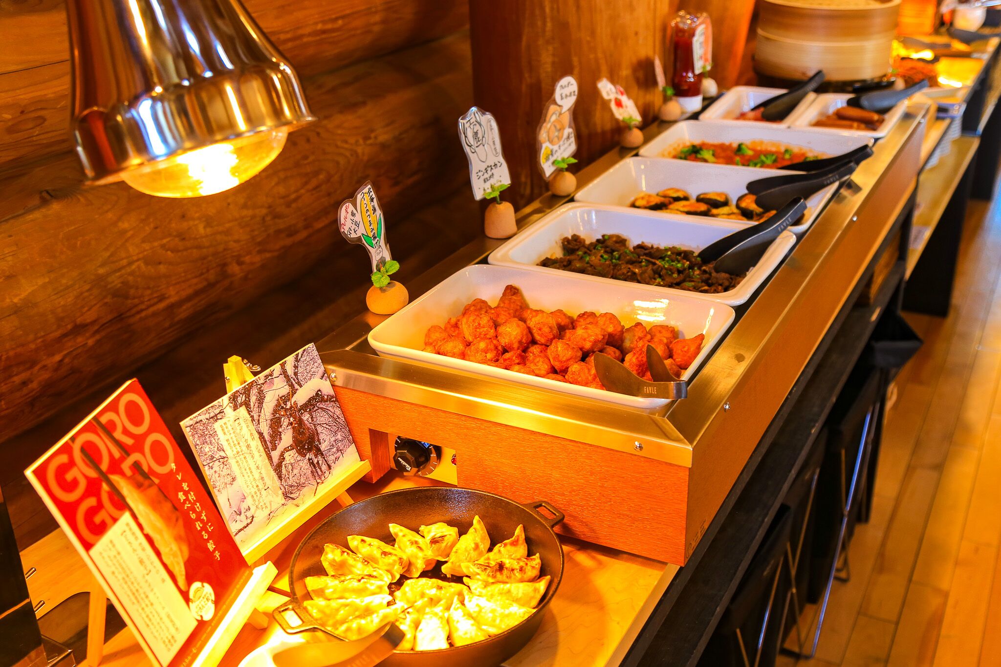 Buffet com diversos pratos, incluindo dumplings e uma placa com texto em japonês.