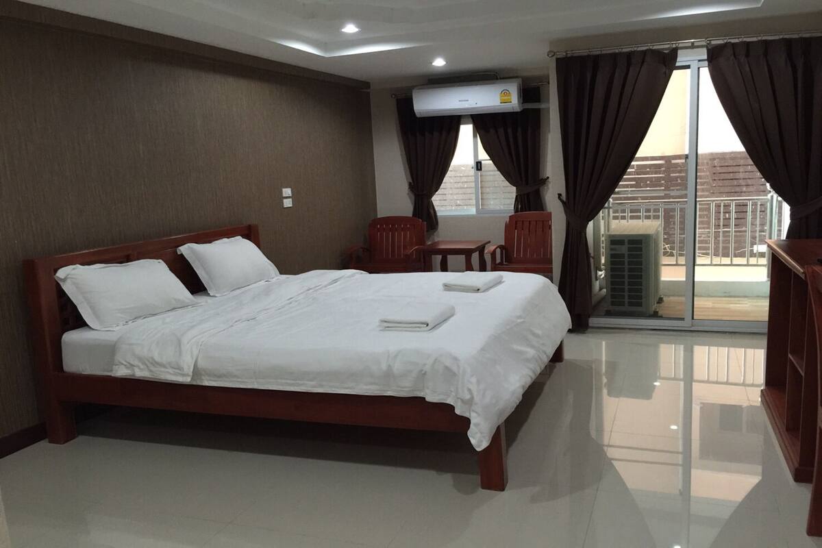 Quarto de hotel com cama de madeira, roupa de cama branca, uma mesinha, duas cadeiras e uma porta de vidro deslizante para o exterior.