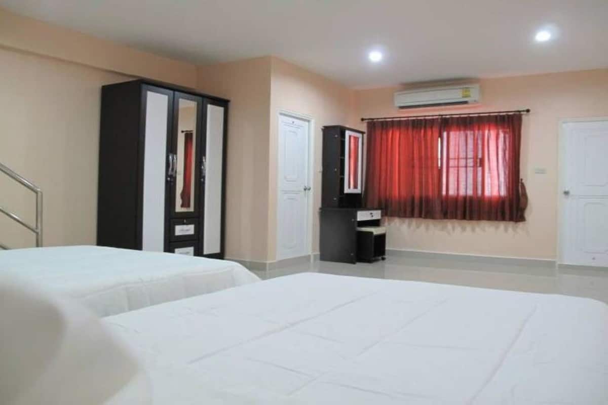 Quarto de hotel com duas camas, um guarda-roupa, uma escrivaninha e uma janela com cortinas vermelhas.