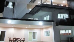 A multi-story building with balconies, large windows, and a dining area with chairs.