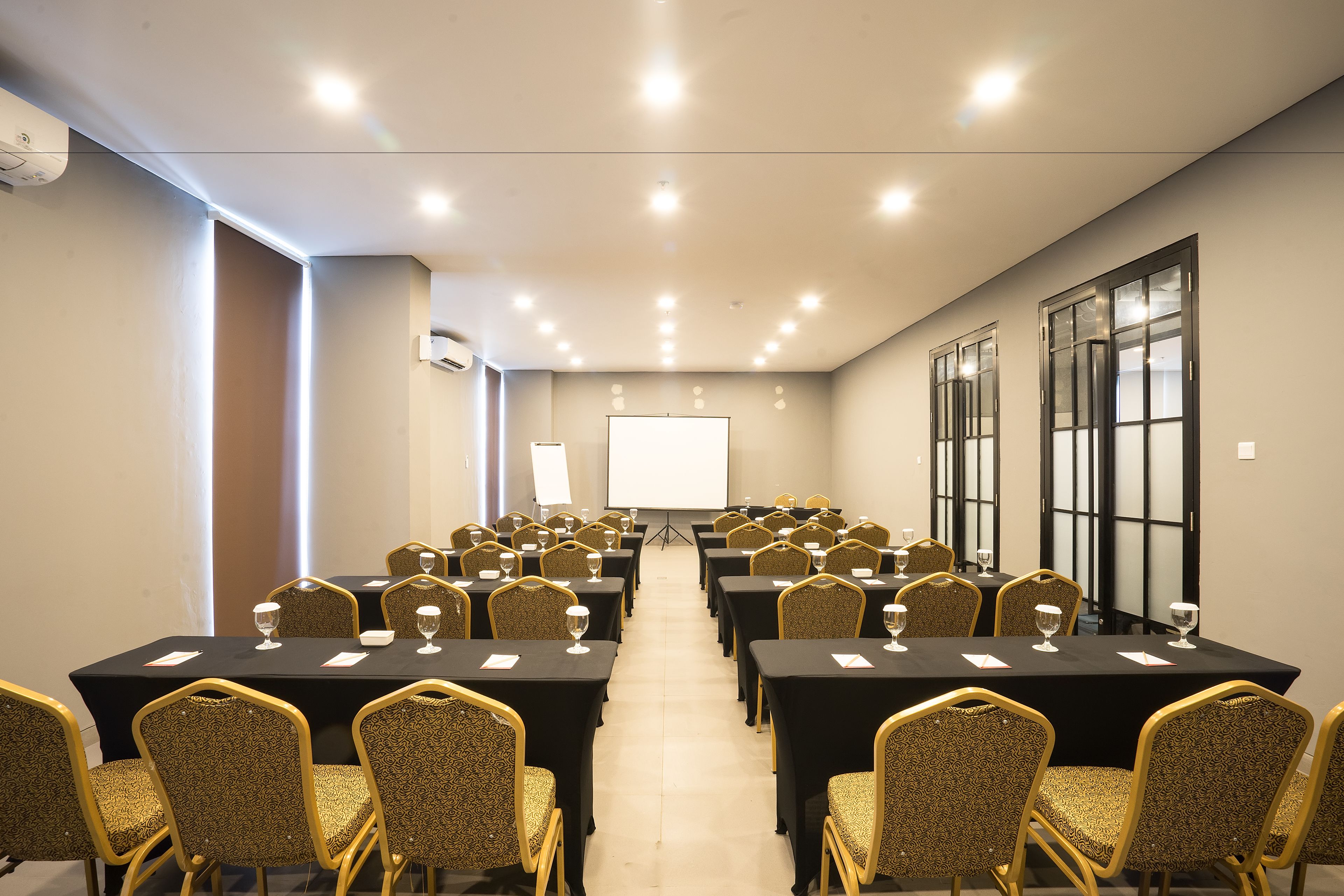 Ein Konferenzraum mit Tischen, Stühlen, einer Projektionsleinwand und einem großen Fenster.