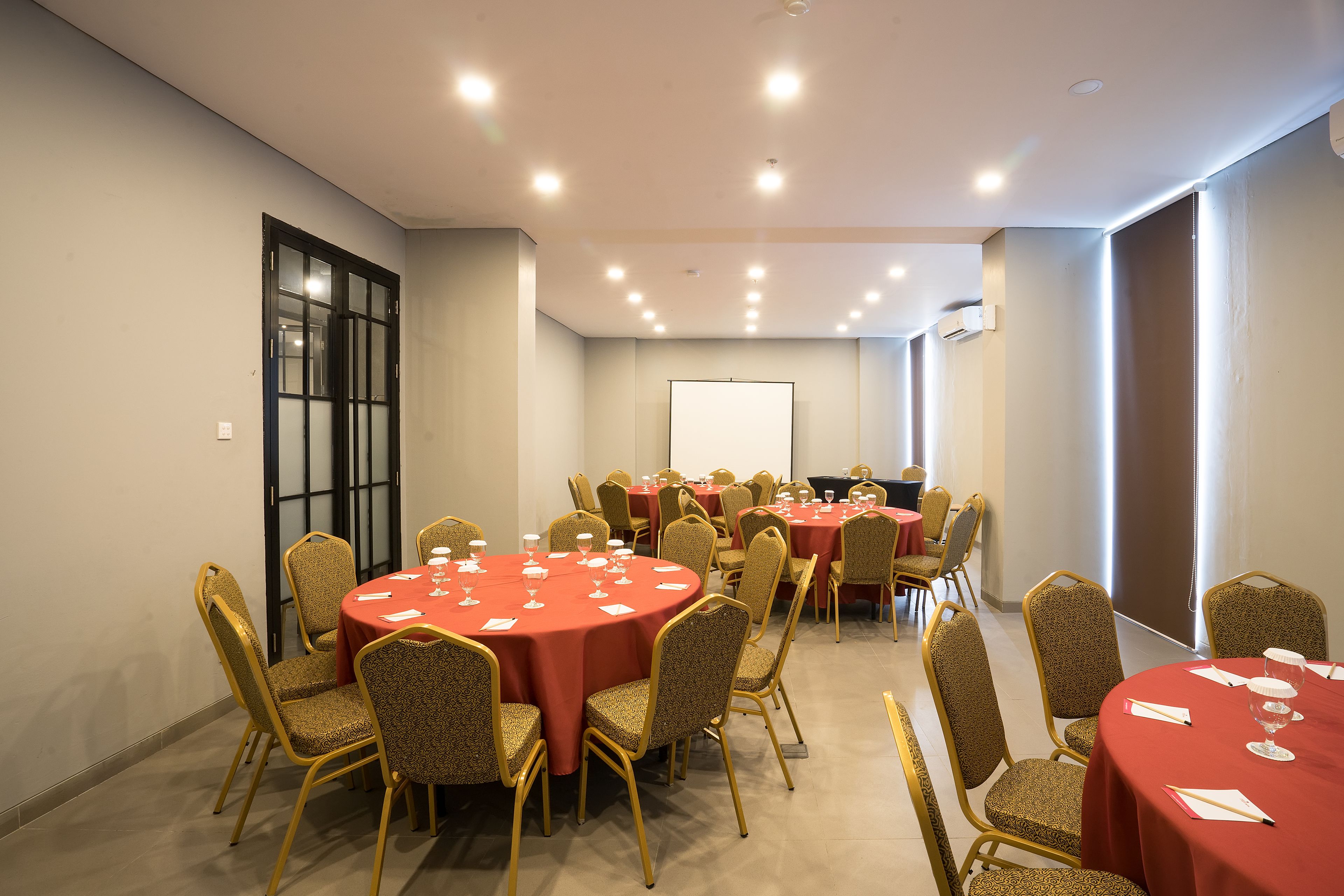 Une salle de conférence dotée de plusieurs tables et chaises, et équipée de tables, de chaises et d’un écran de projection.