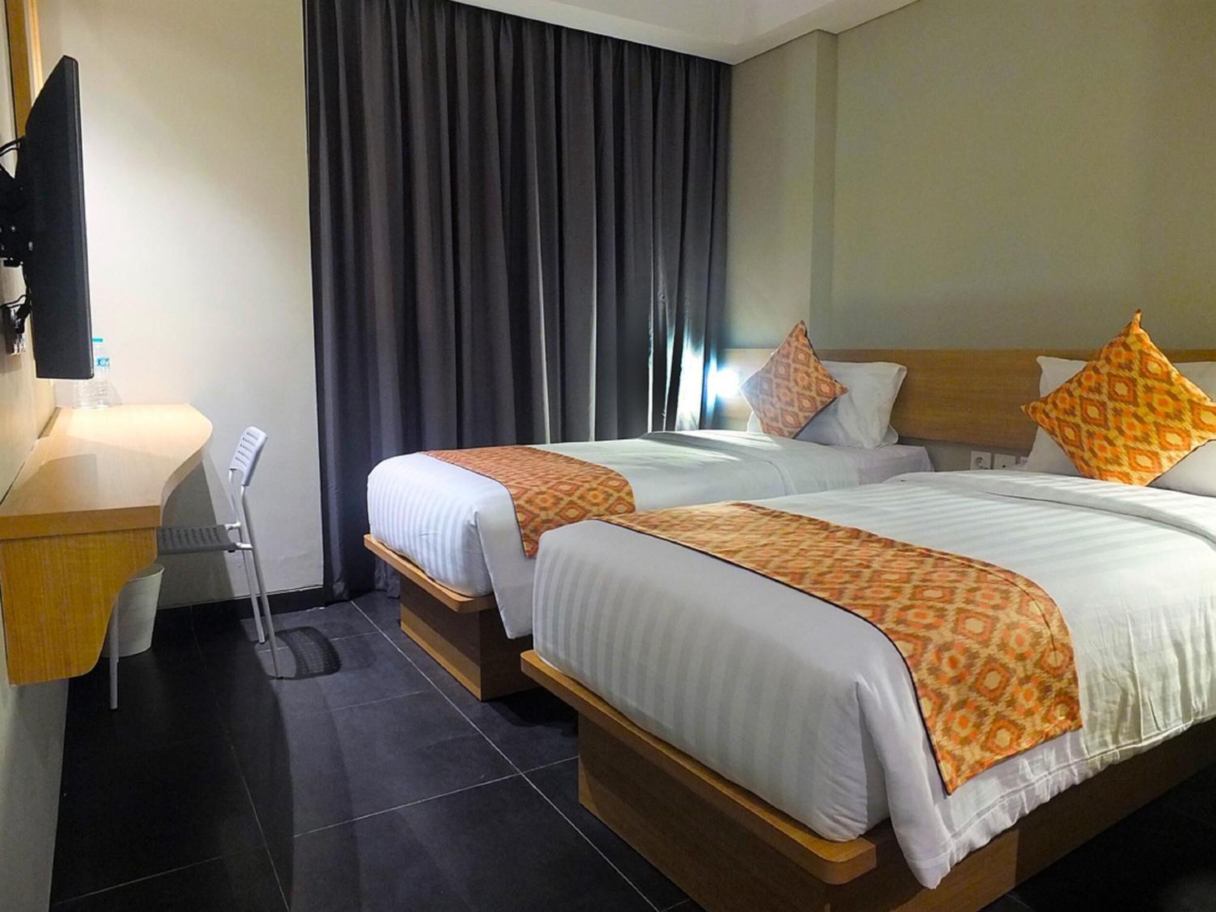 Une chambre d’hôtel avec deux lits, un bureau, une chaise, une télévision et une grande fenêtre avec des rideaux.