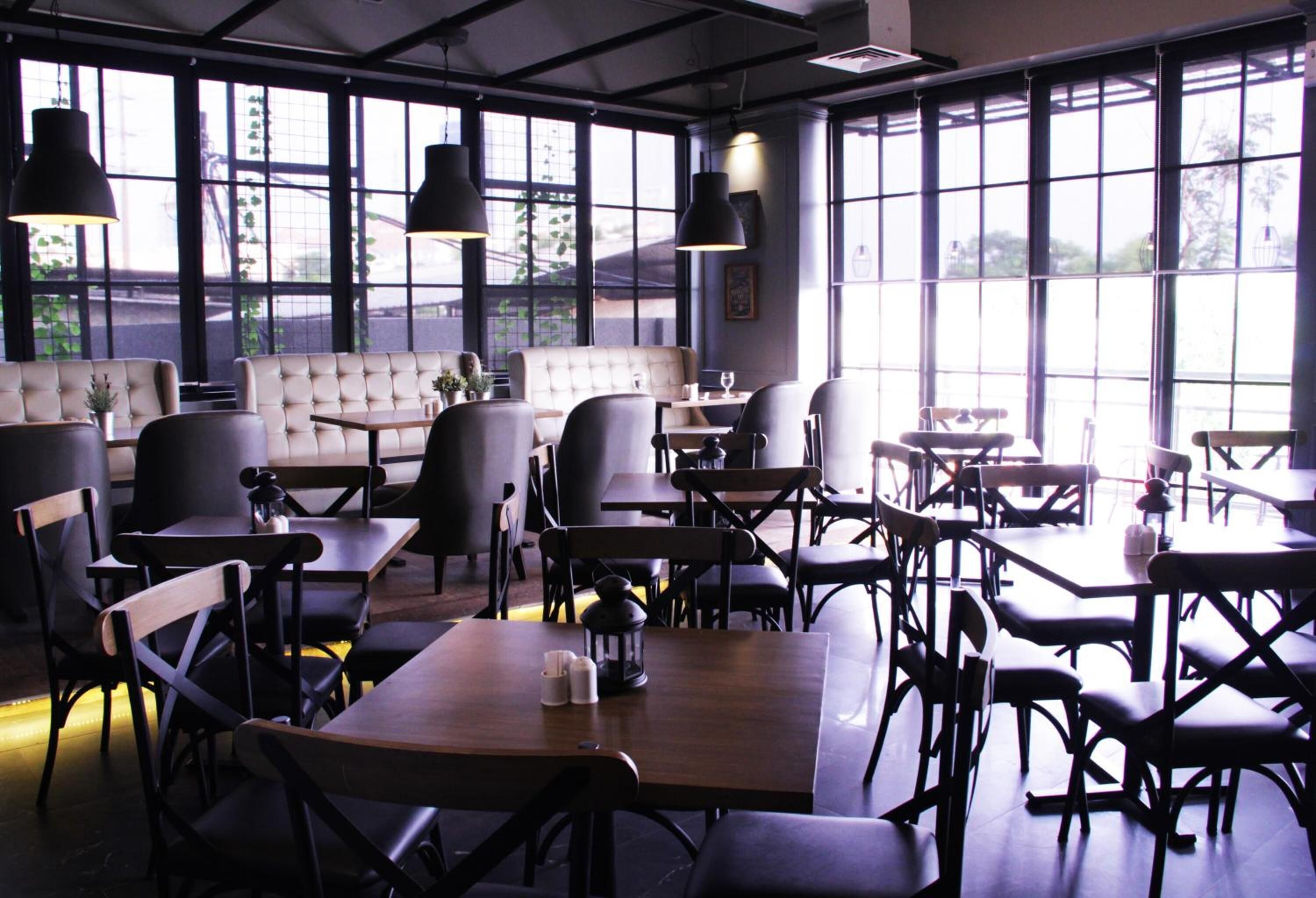 Een restaurant met hoge plafonds, grote ramen en diverse zitmogelijkheden, waaronder tafels en zitbanken.