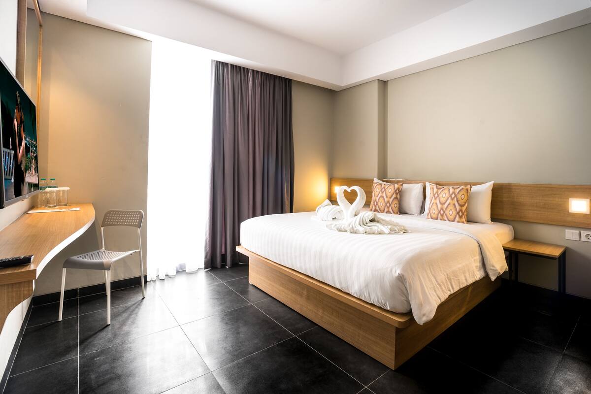A modern hotel room with a wooden bed, a desk, and a chair.