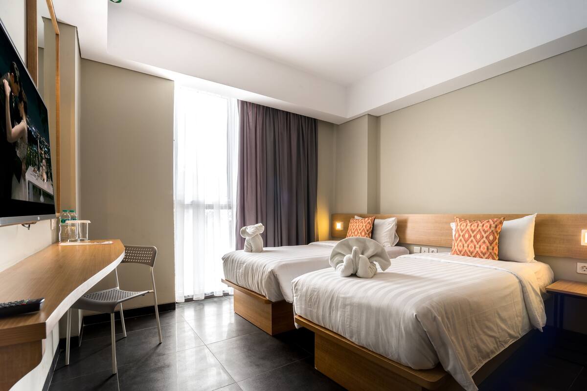 A hotel room with two beds, a desk, and a chair.