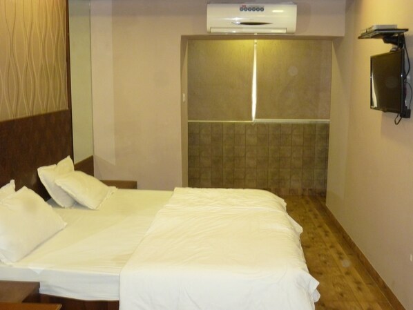 A hotel room with a bed, a wall-mounted phone, and an air conditioning unit. - Hotel Regal Palace (Mumbai)