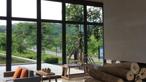 Ein geräumiges Zimmer mit großen Fenstern, einem modernen Sofa, einem Holztisch und einem Holzstapel.