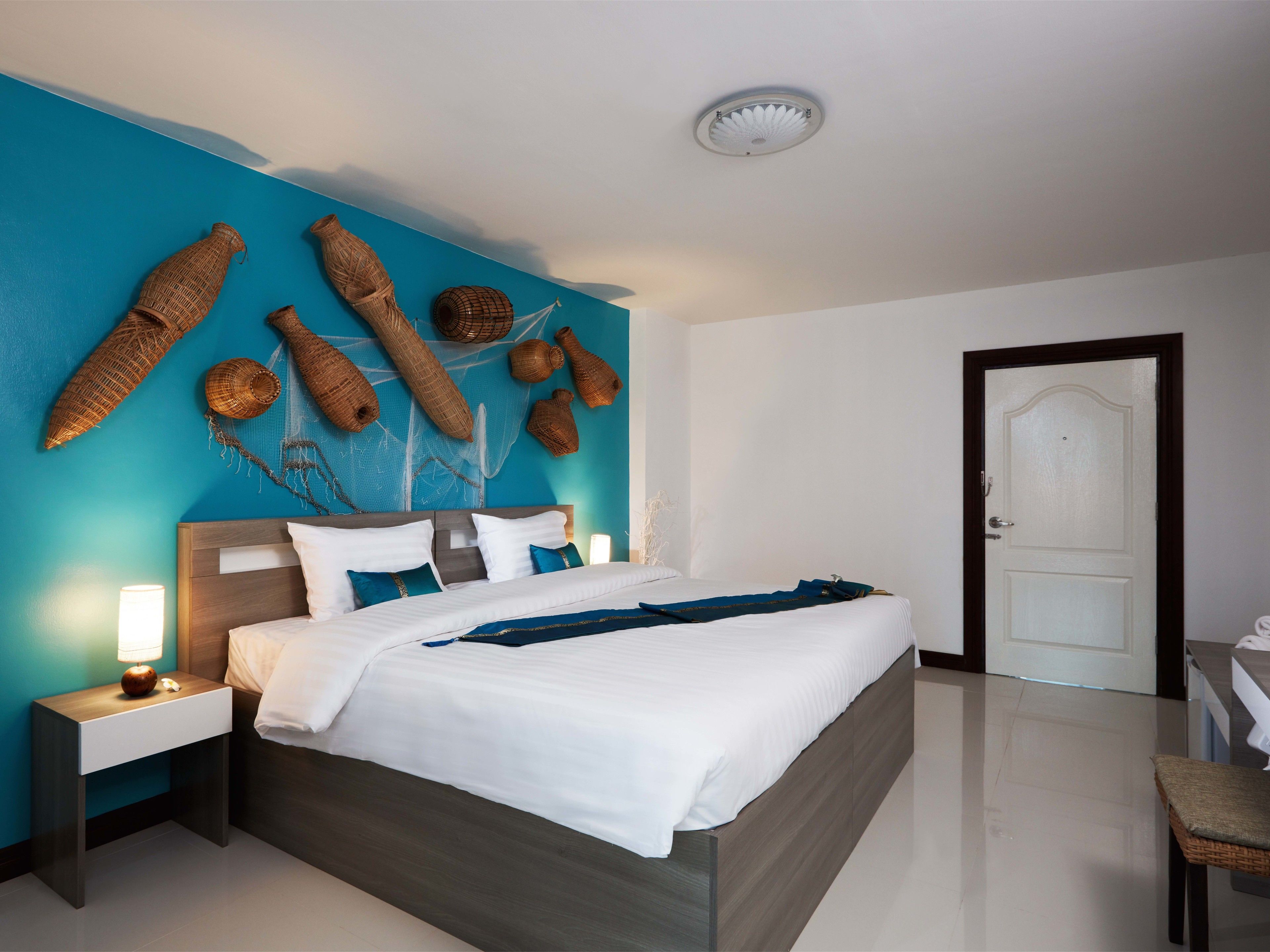A modern hotel room with a large bed, a nightstand with a lamp, and a door.