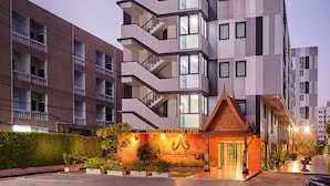 Un hotel moderno con un llamativo elemento arquitectónico tailandés, varios balcones y un jardín bien cuidado.