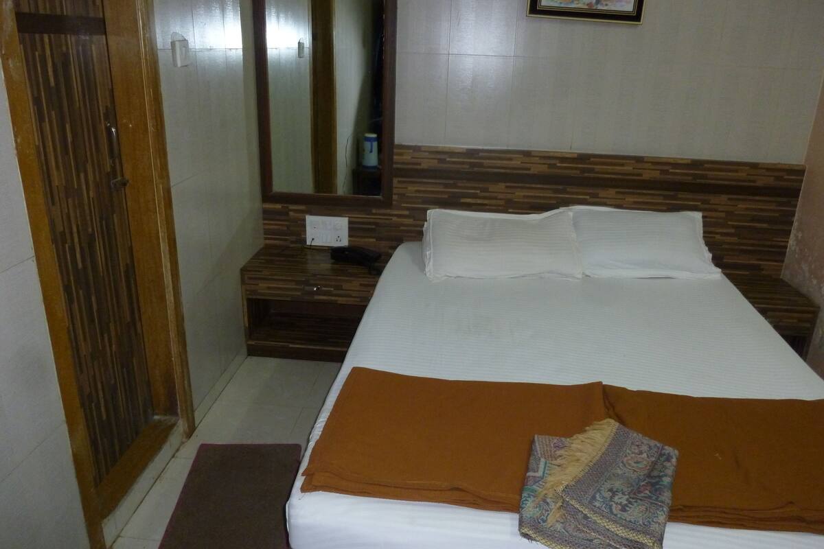 A hotel room with a bed, a wooden nightstand, a mirror, and a wall-mounted picture.