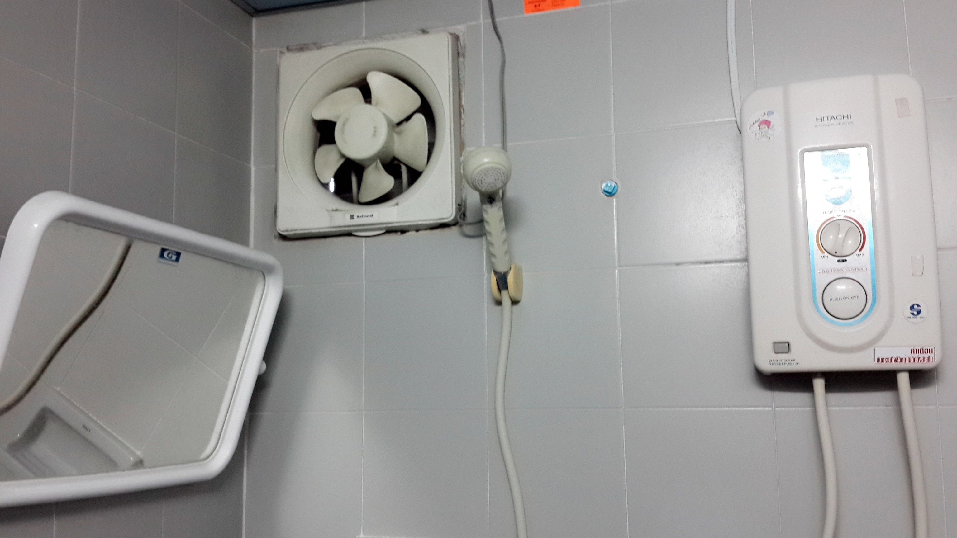 A bathroom with a white fan, a heater, and a shower control panel.
