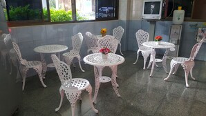 Una habitación con sillas y mesas de metal blanco dispuestas en círculo. Se ve vegetación a través de la ventana.