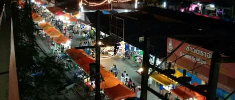 Un mercado al aire libre concurrido, con numerosos puestos y sombrillas naranjas, ubicado en una zona urbana de noche.