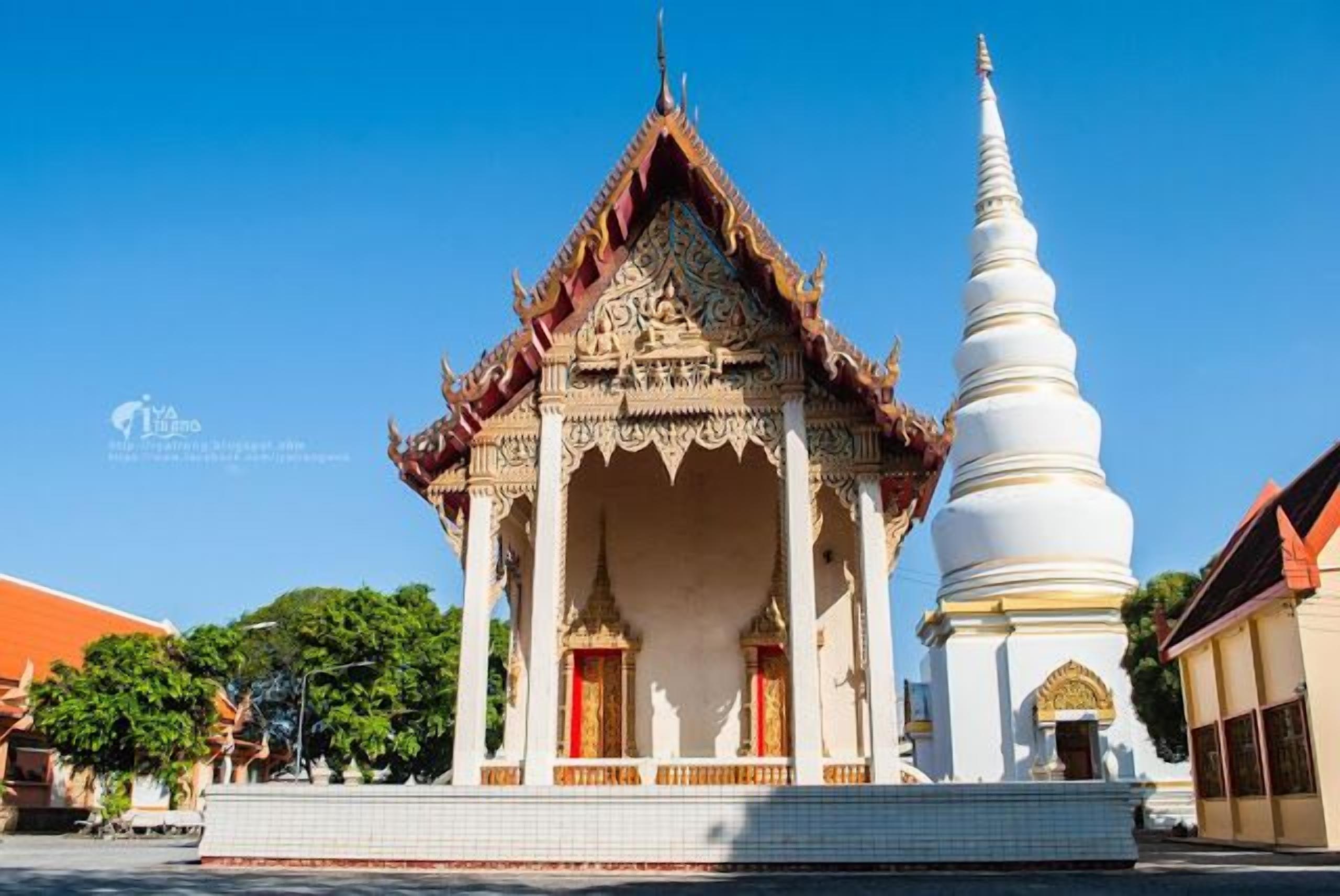 Un temple thaïlandais traditionnel, doté d’un sanctuaire central et d’une haute stupa blanche.