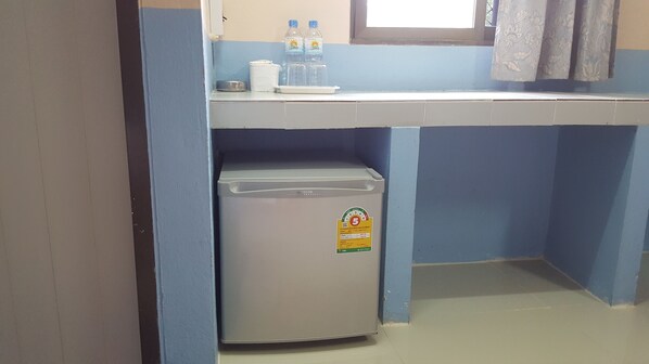 A compact room with a small refrigerator, a water dispenser, and a window with curtains.