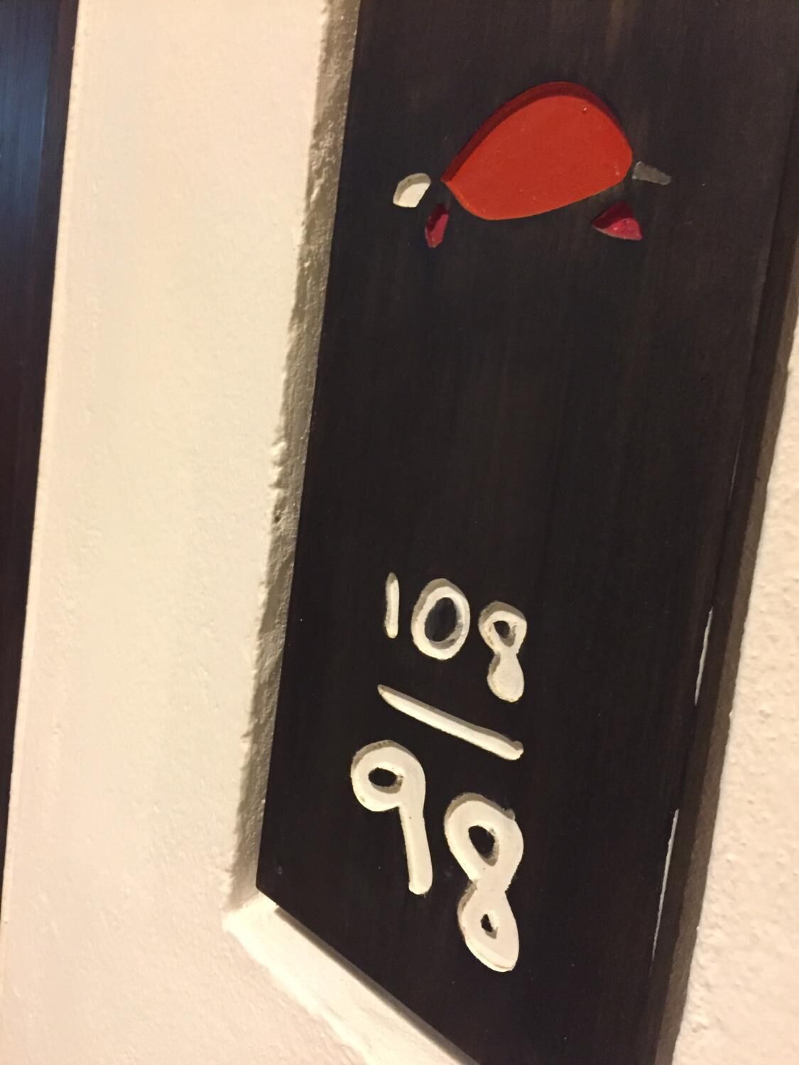 Een zwarte deur met witte cijfers '108' en '98' en een rood voorwerp erboven.