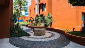 A courtyard with a circular stone feature, surrounded by greenery and a building with orange walls. - Away Las Tortugas Beachfront (Hua Hin)
