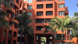 A modern multi-story building with balconies, surrounded by palm trees and a water feature. - Away Las Tortugas Beachfront (Hua Hin)